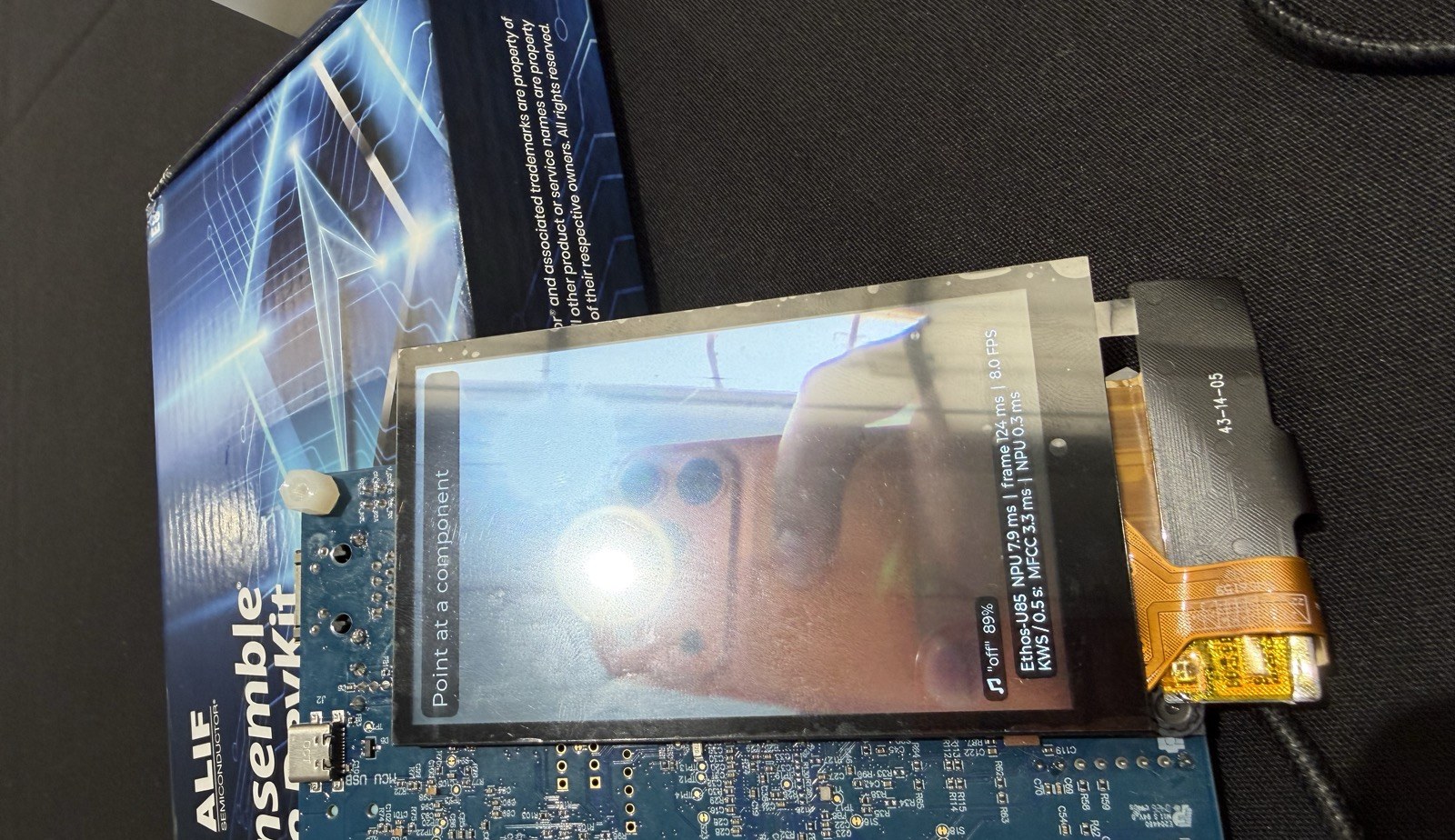 The Alif E8 DevKit running DCSM-Simplified; the LCD footer reads NPU 7.9 ms, frame 124 ms, 8.0 FPS, and keyword spotting MFCC 3.3 ms, NPU 0.3 ms